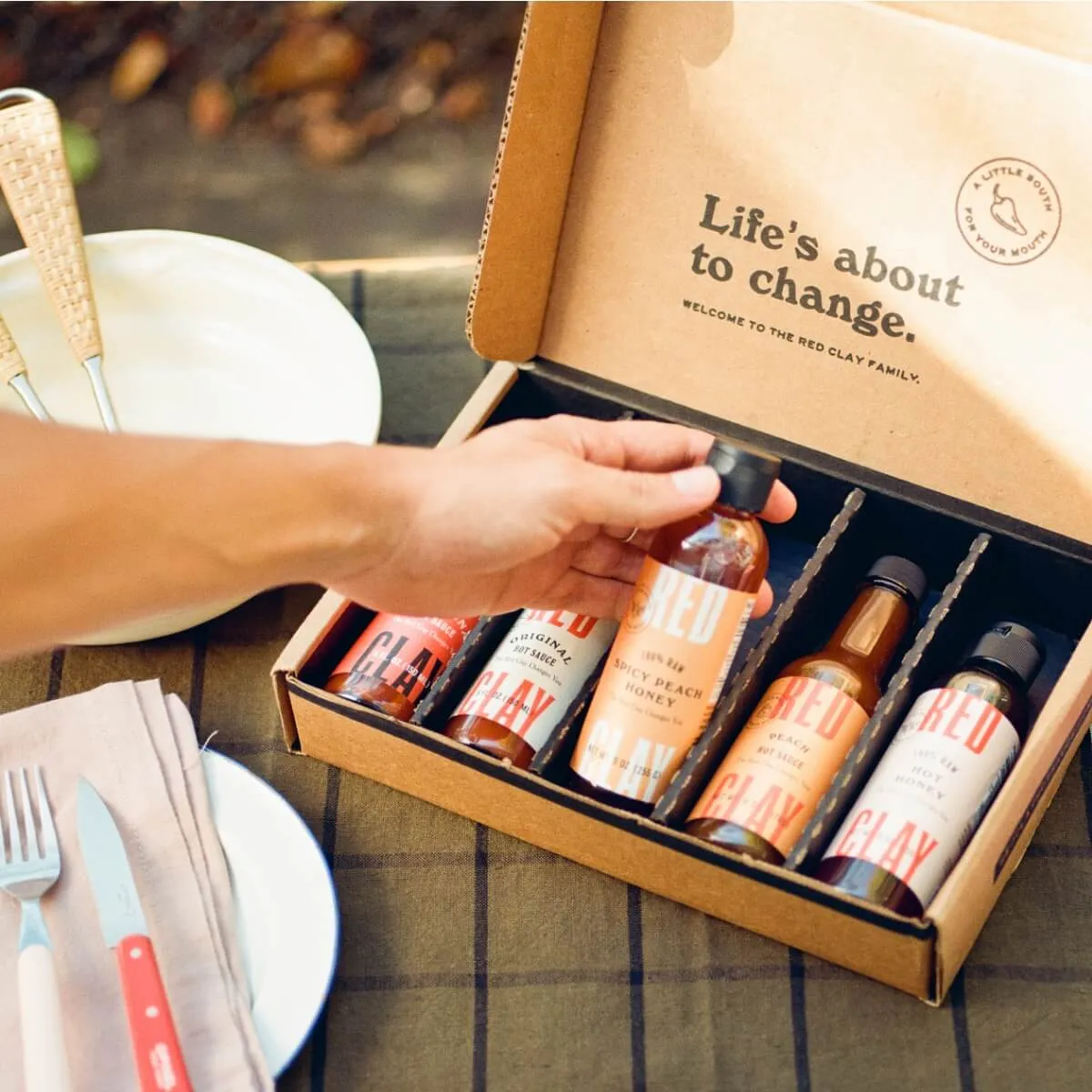 A hand lifting a bottle out of a Red Clay gift box