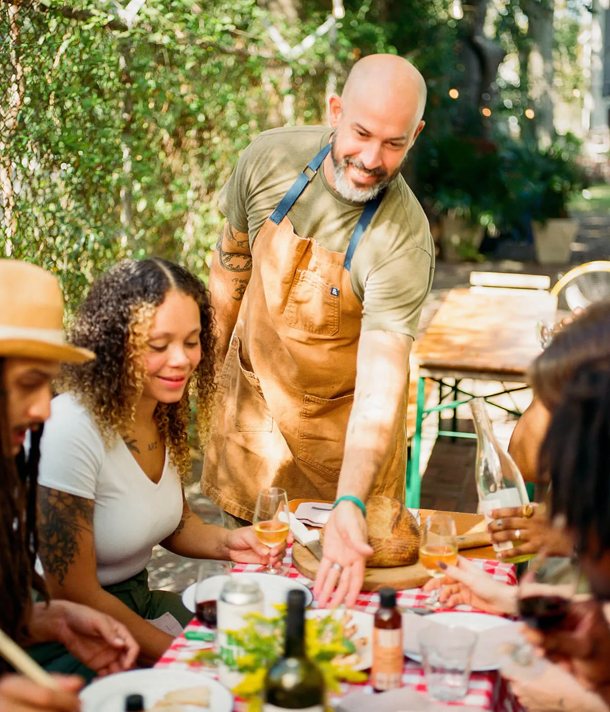 A chef serving guests at a long outdoor dinner table