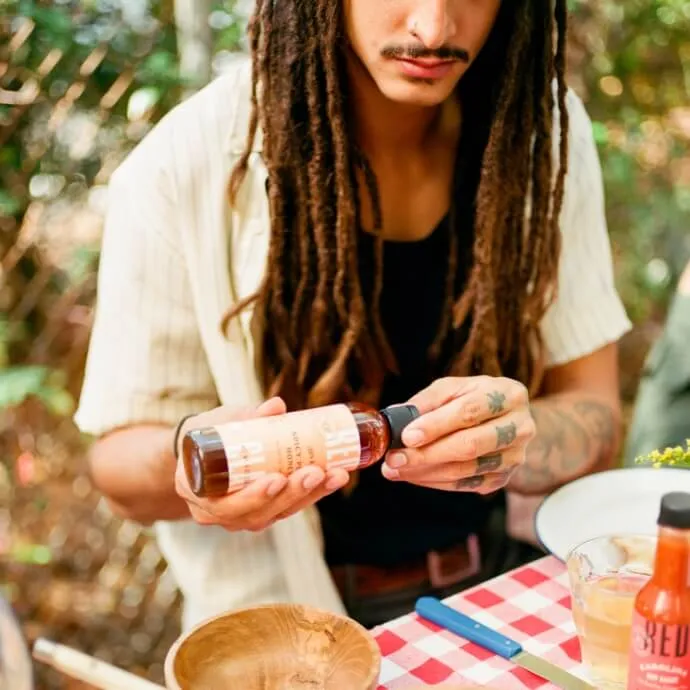 A cook shaking Red Clay hot sauce over a plate